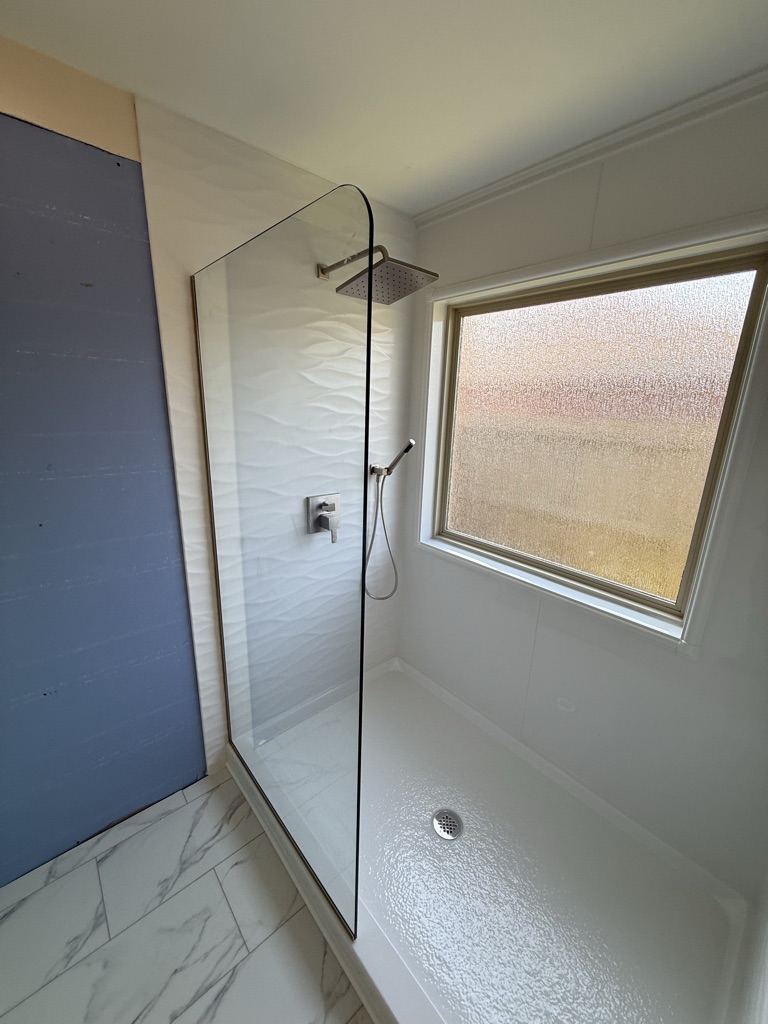 Walk in shower with a frameless glass panel, wave pattern walls and a rain shower head