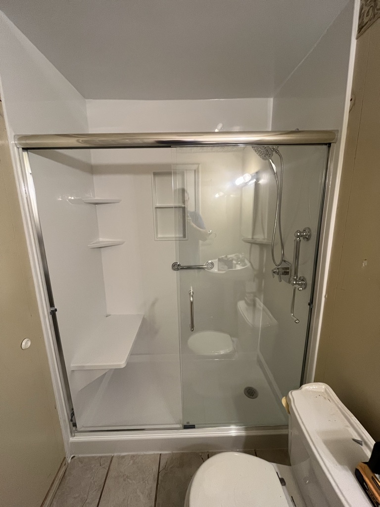 White walk in shower with a built in bench, corner shelves, grab bar and sliding glass door