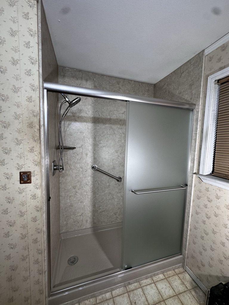 Walk in shower with a frosted sliding door, a grab bar and a handheld shower head