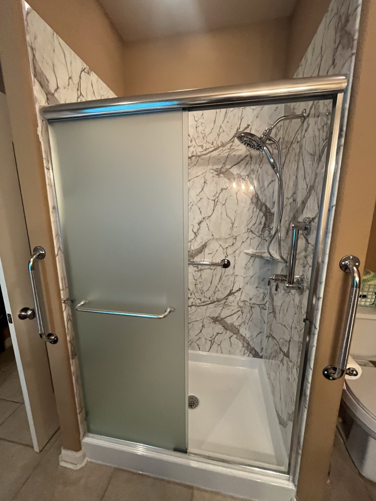 Shower with marble look walls, a frosted sliding door and grab bars inside and out