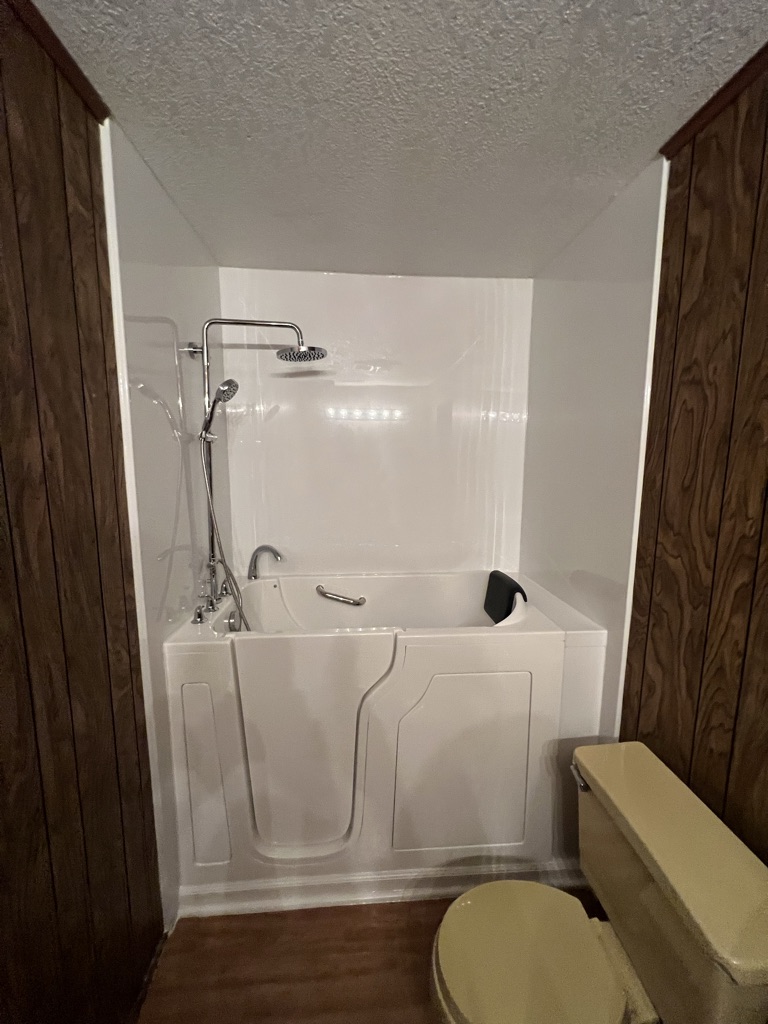 Walk in tub with a low entry door, a headrest and a shower head on a riser bar