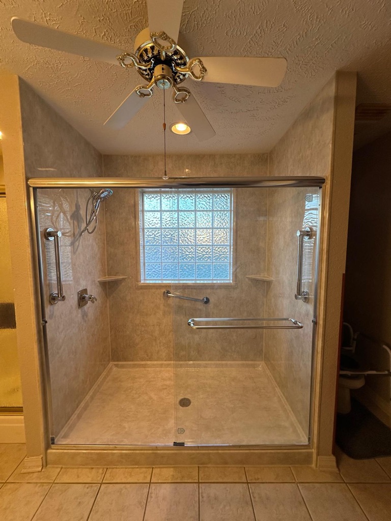 Large walk in shower with stone look walls, a glass block window, grab bars and a sliding glass door