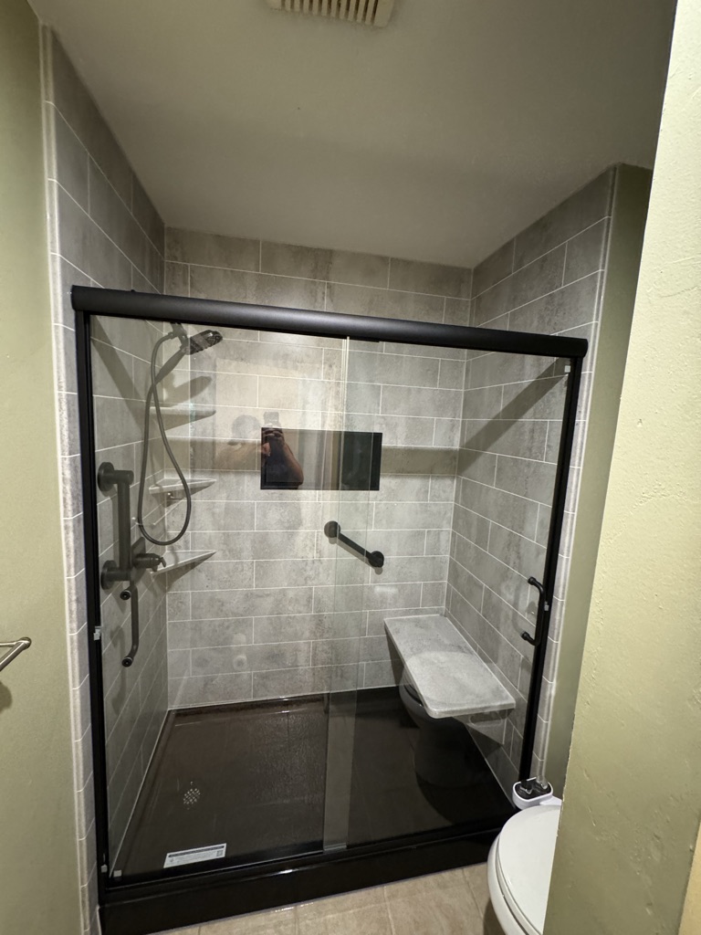 Walk in shower with gray patterned walls, a fold down seat, a grab bar and a black framed glass door