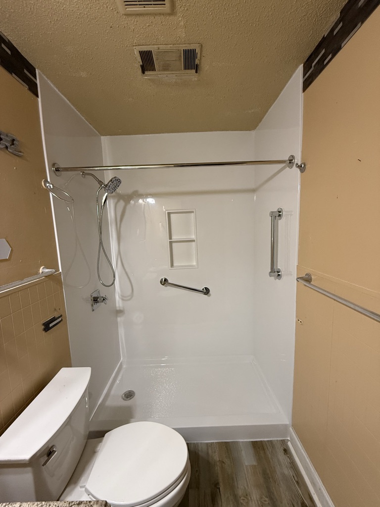 White walk in shower with a niche, a handheld shower head and two grab bars