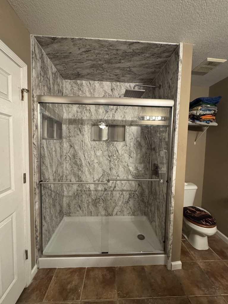 Walk in shower with gray marble look walls, two niches and a sliding glass door