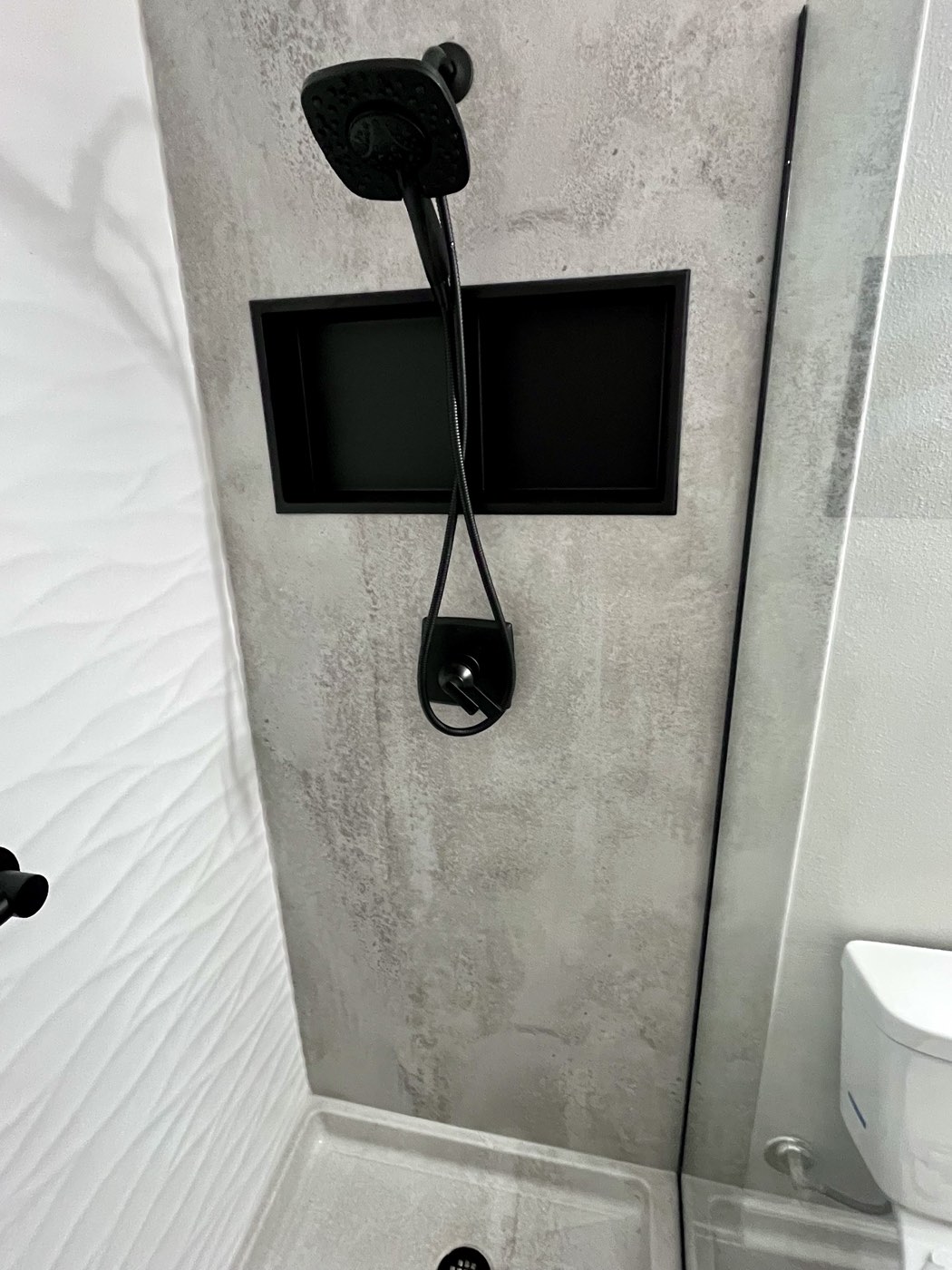 Shower detail with a black handheld shower head and a black recessed niche on a concrete look wall