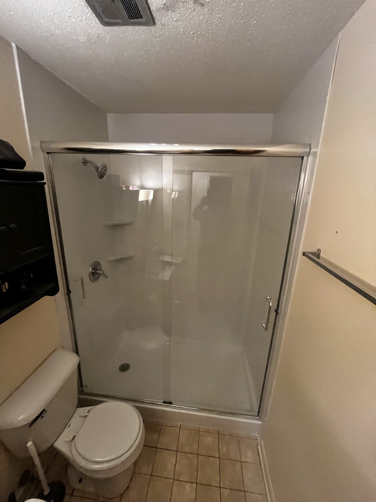 White walk in shower with corner shelves and a chrome sliding glass door