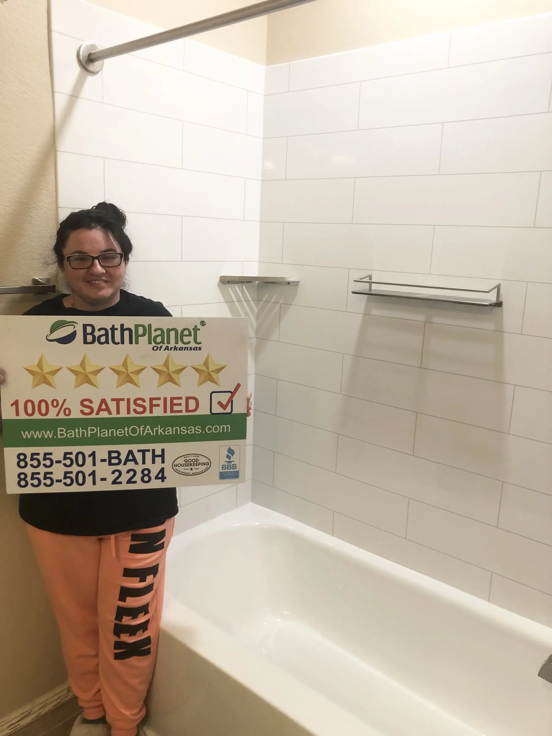 Homeowner holding a 100% Satisfied sign beside her new bathtub and walls
